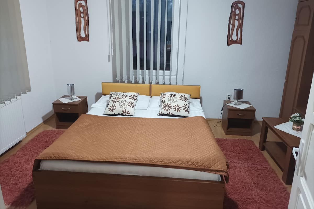 Un dormitorio ordenado con cama, dos mesitas de noche, una ventana con persianas y decoración en la pared.