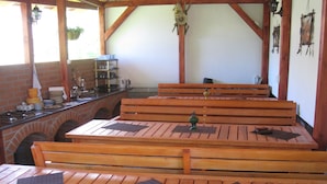 Un espacio al aire libre con bancos y mesas de madera, un muro de ladrillo y una planta colgante.