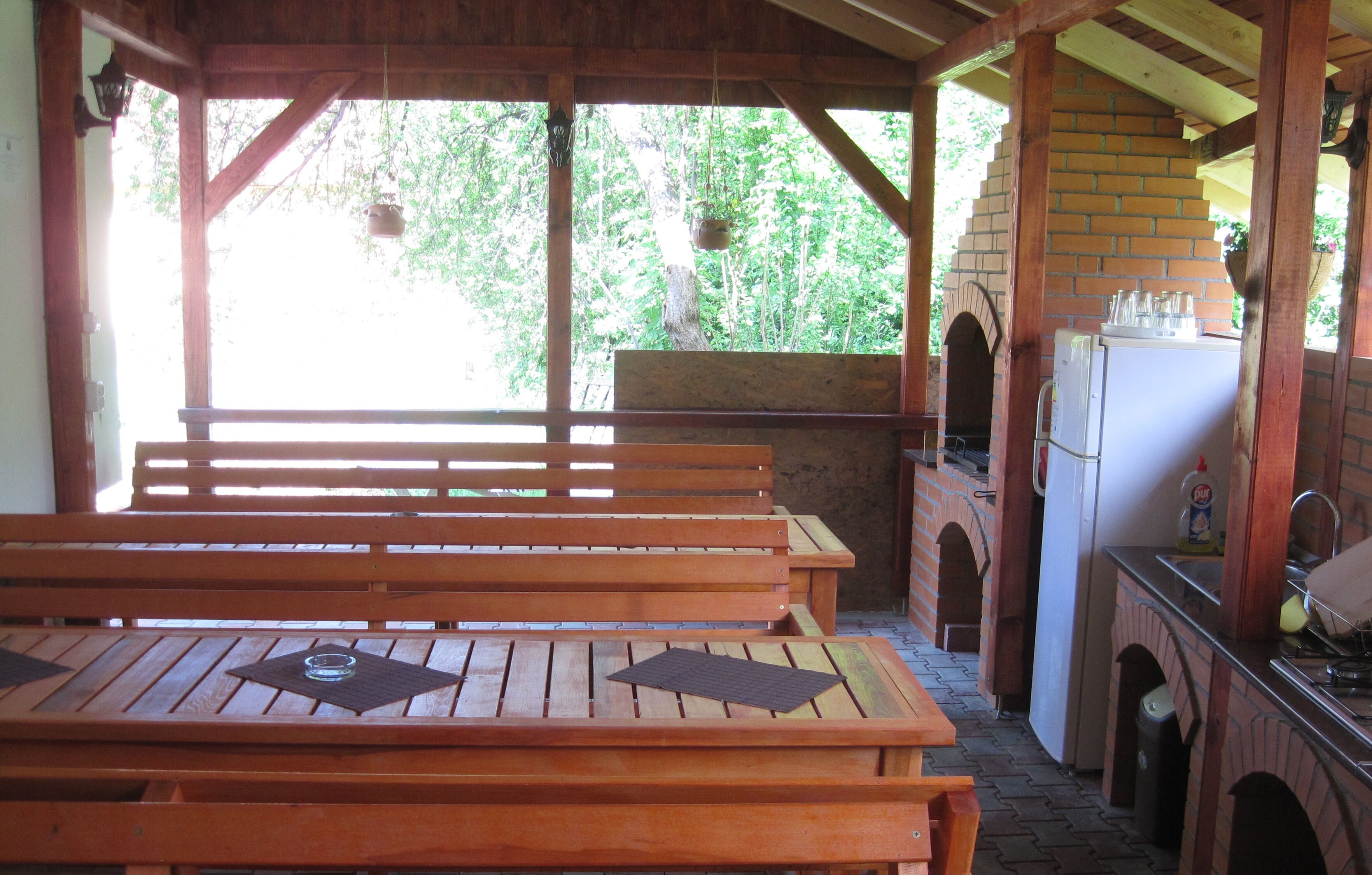 A covered outdoor seating area with wooden benches and a brick oven.