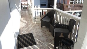 A balcony with wicker furniture, a tiled floor, and a view of buildings in the background.