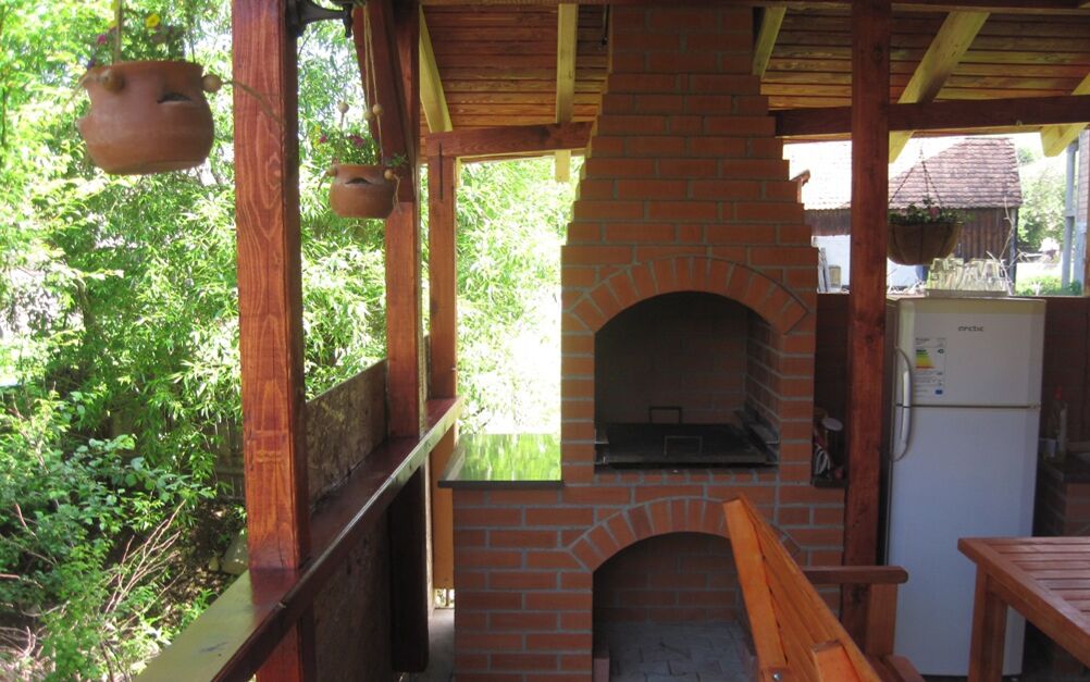 A rustic outdoor kitchen with a brick oven, wooden furniture, and hanging pots.