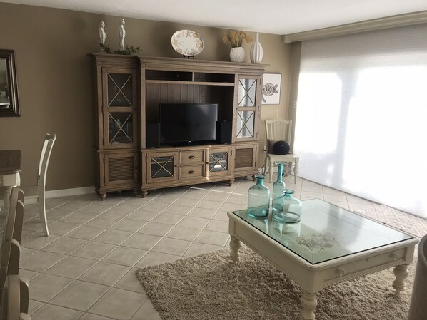 A living room with a television on a wooden cabinet, a glass coffee table with decorative items, and a large window. - Longboat Key with Gulf to Bay access. Beautiful view of Bishop's Bayou. (Longboat Key)