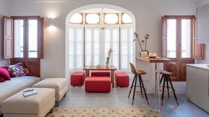Un salon moderne comprenant un canapé, des poufs, une table à manger avec des chaises et un coin cuisine.