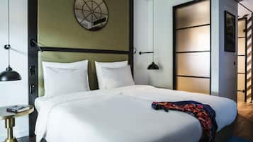 A neatly made bed with white linens, a round wall decoration, and a large window with a view.