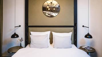 A hotel room with a bed, two bedside tables, a mirror on the wall, and two pendant lights.