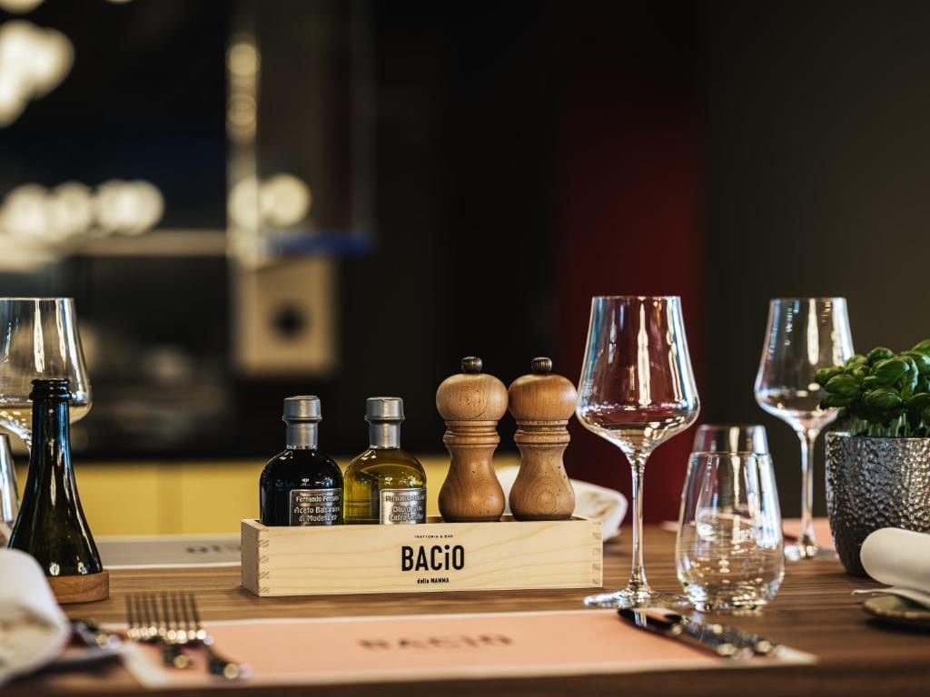 A dining table with a wooden box labeled 'BACIO,' various bottles, and wine glasses.