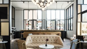 Zona de bar moderna con sofá y sillas, ventanas amplias y barra repleta de botellas.