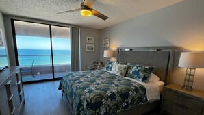 A hotel room with a bed, a nightstand, a desk, a chair, a balcony with a view of the ocean, and a ceiling fan. - Beachfront Sky High Views-14th Floor- Sand Key! Resort Level Amenities! (Clearwater)