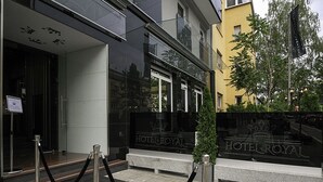 Een moderne hotelentree met een glazen gevel, een bord met 'HOTEL ROYAL' en een zwarte touwbarier.