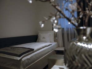 A hotel room with a bed, a nightstand, a vase with branches, and a window with curtains. - Hotel Royal (Karlsruhe)