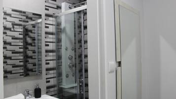 Un baño moderno con cabina de ducha de vidrio, un lavamanos blanco con dispensador de jabón y un espejo con un respuesto de blanco y negro.
