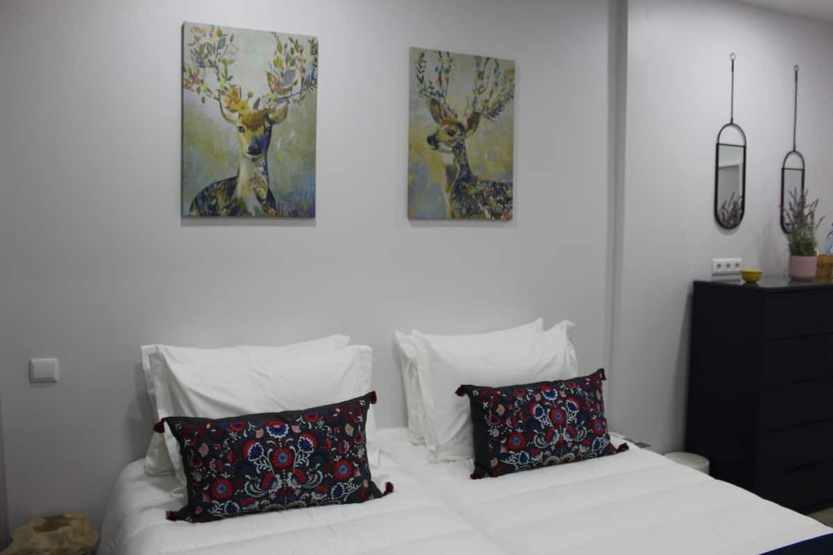 A bedroom with a bed, two decorative pillows, a dresser, and two wall-mounted mirrors.