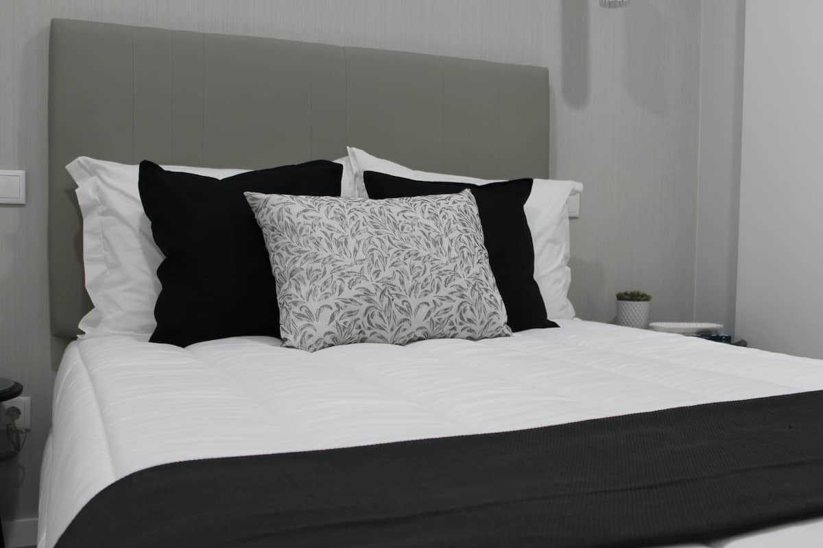 A neatly made bed with a grey headboard, white and black pillows, and a black throw blanket.