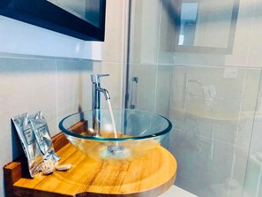 Bathroom features a clear glass sink, shower enclosure, and mirror.