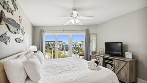 Une chambre d’hôtel avec un grand lit, un ventilateur de plafond, une télévision et un balcon donnant sur les bâtiments.