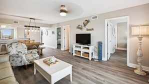 Un salon moderne avec une table basse blanche, un canapé à motifs et un téléviseur posé sur un meuble blanc.