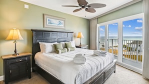 A hotel room with a large bed, two bedside tables with lamps, a ceiling fan, a view of the ocean, and a balcony with a railing. - Seacrest 703 is a 2 BR Gulf Front on Okaloosa Island by RedAwning (Fort Walton Beach)