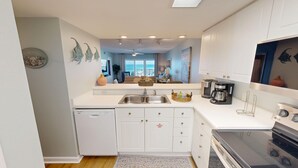 A modern kitchen with white cabinetry, a double sink, a coffee maker, and a dishwasher. - Seacrest 702 is a Gulfview 2 BR on Okaloosa Island by RedAwning (Fort Walton Beach)
