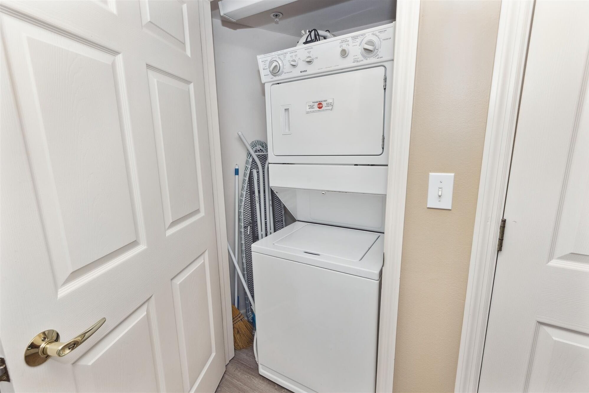 A laundry room with stacked washers and dryers, a broom, and a mop.