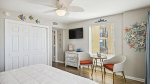 Un dormitorio con una cama, un ventilador de techo, un televisor, un aparador y una ventana con persianas.