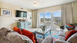 A living room with a sofa, a coffee table, and a TV. There is a balcony with a view of the city. - Seacrest 511 is a Gulf side 2 BR on Okaloosa Island by RedAwning (Fort Walton Beach)