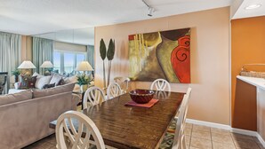 Un salon moderne avec un coin repas, comprenant une table à manger en bois, des chaises blanches et un grand tableau abstrait accroché au mur.