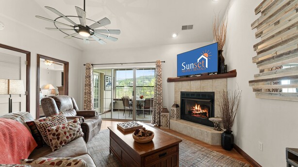 A living room with a fireplace, a television mounted on the wall, and a ceiling fan.