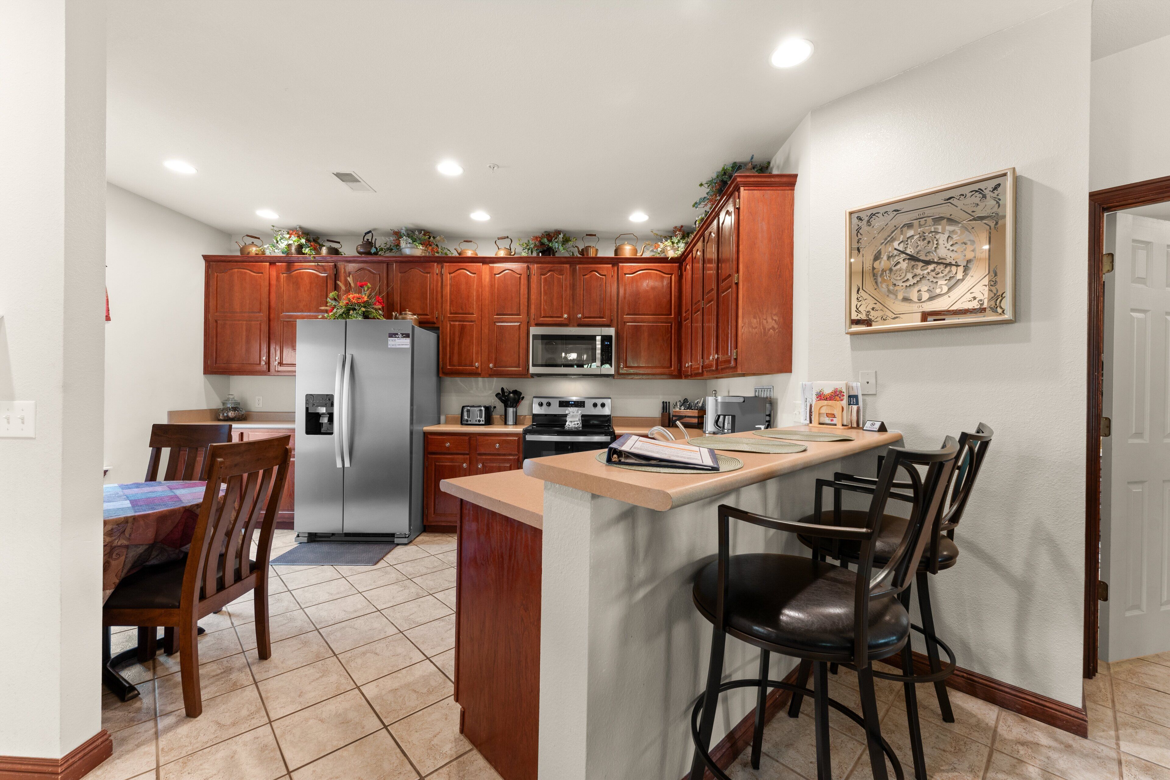 Una cocina con armarios de madera, un refrigerador, un microondas y un comedor con sillas y una mesa.