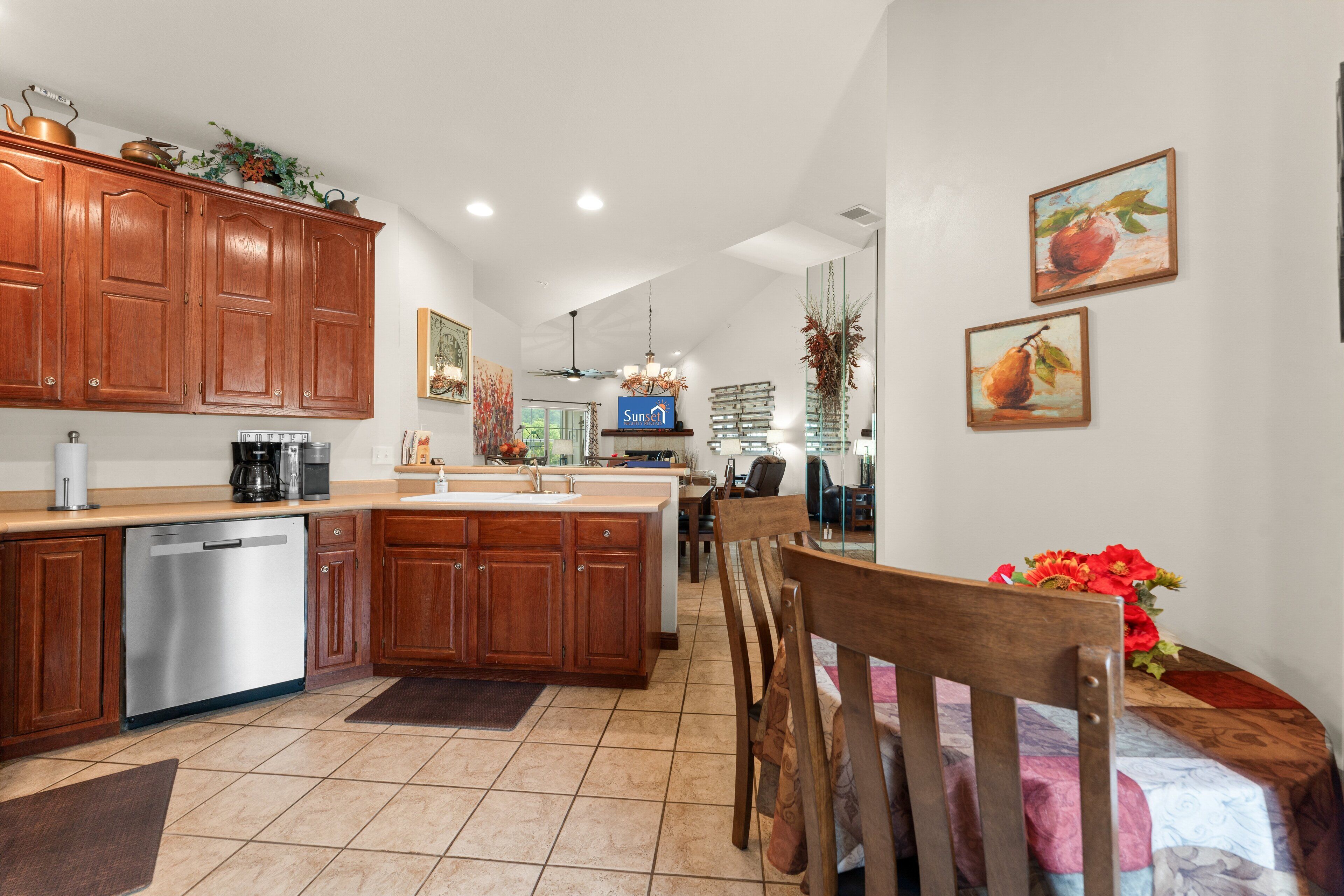 A kitchen with wooden cabinets, a dishwasher, a coffee maker, and a dining area with a table and chairs.