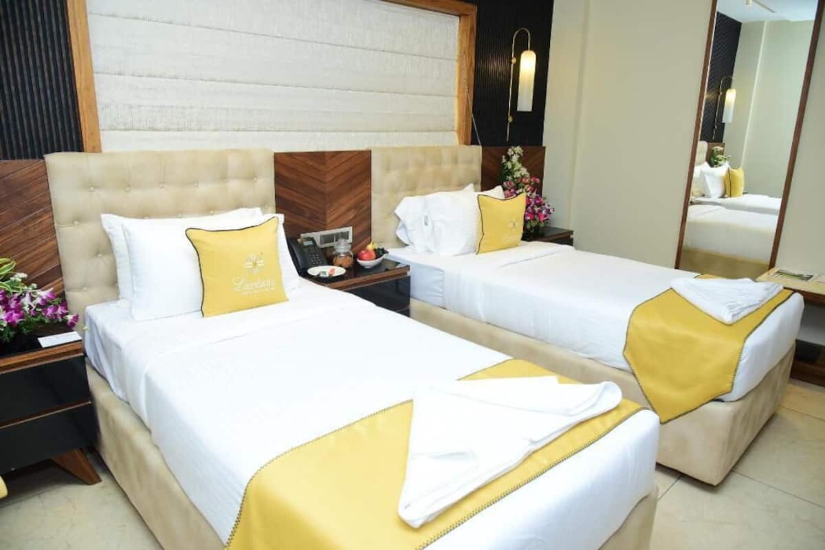 A hotel room with two beds, each with a white and yellow bedspread, a wooden headboard, and a nightstand with a phone and a small table with a vase of flowers.