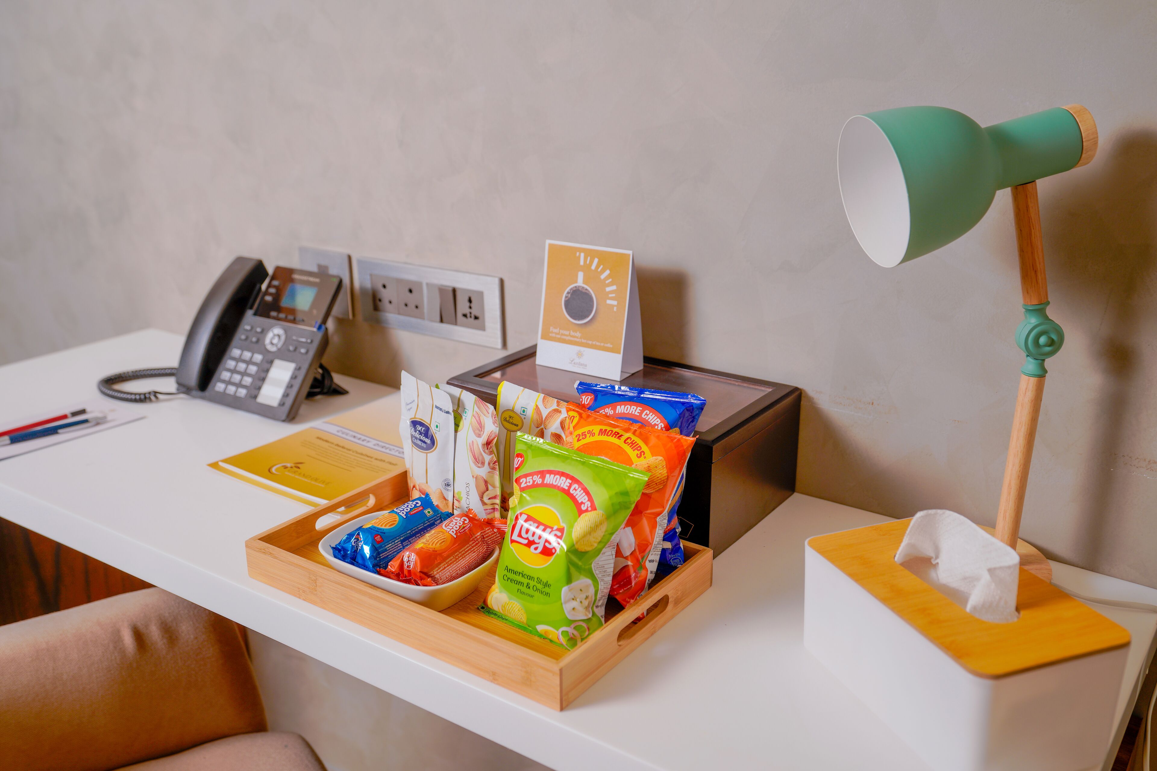 A hotel reception desk with a telephone, a sign, a tray with snacks, and a desk lamp.