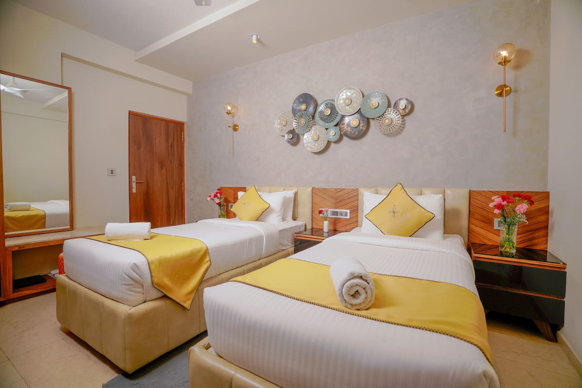A hotel room with two beds, a large mirror, decorative wall plates, and a nightstand with a vase of flowers.