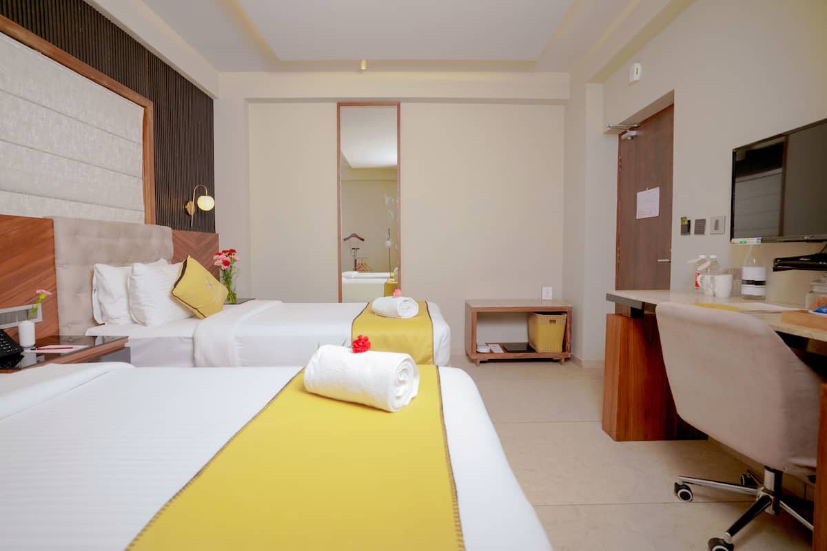 A hotel room with two beds, a desk, a chair, a TV, and a mirror.
