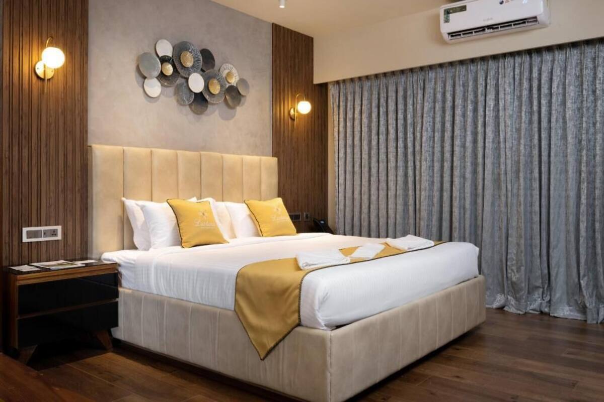 A modern hotel room with a large bed, wooden paneling, a wall-mounted air conditioner, and a curtain on the window.