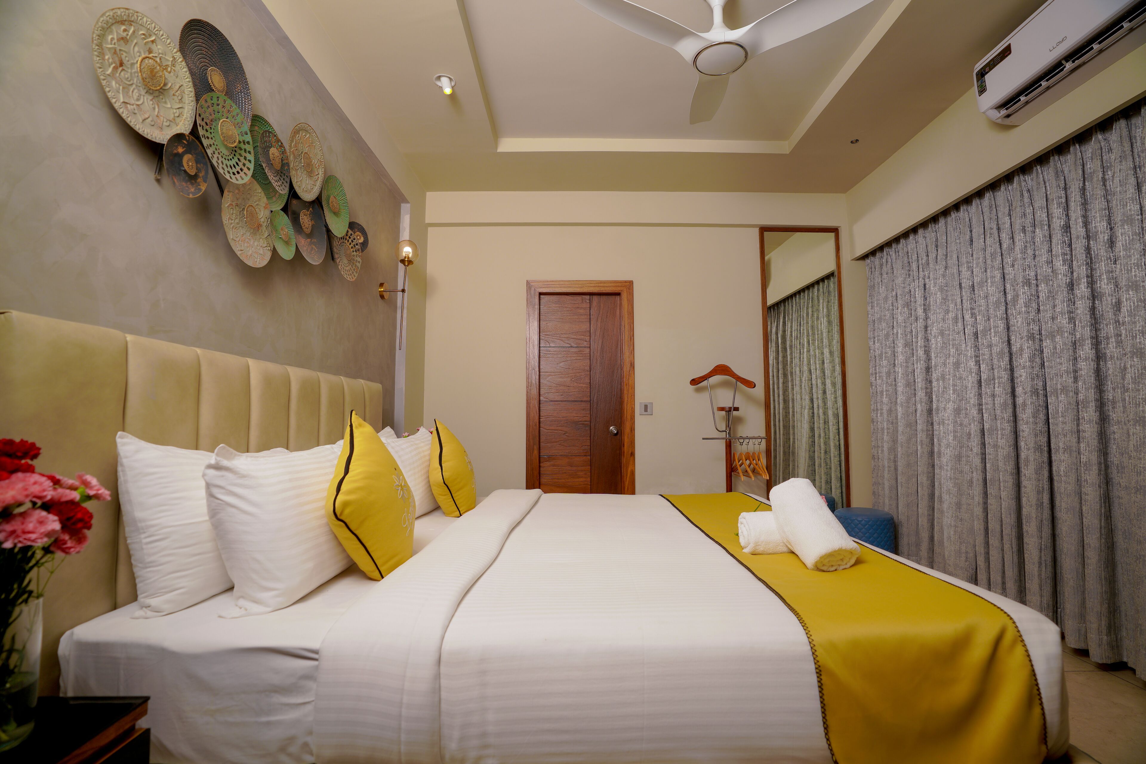 A hotel room with a bed, a ceiling fan, an air conditioning unit, and a door.