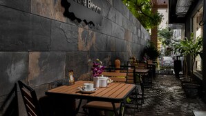 A café with a stone wall and wooden tables, a sign reading "Café Bloom," and potted plants. - Lazdana Hotel Bangalore (Bengaluru)