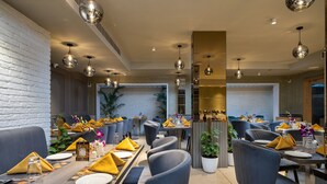 A restaurant with modern decor, featuring grey upholstered chairs, yellow napkins, and pendant lighting. - Lazdana Hotel Bangalore (Bengaluru)