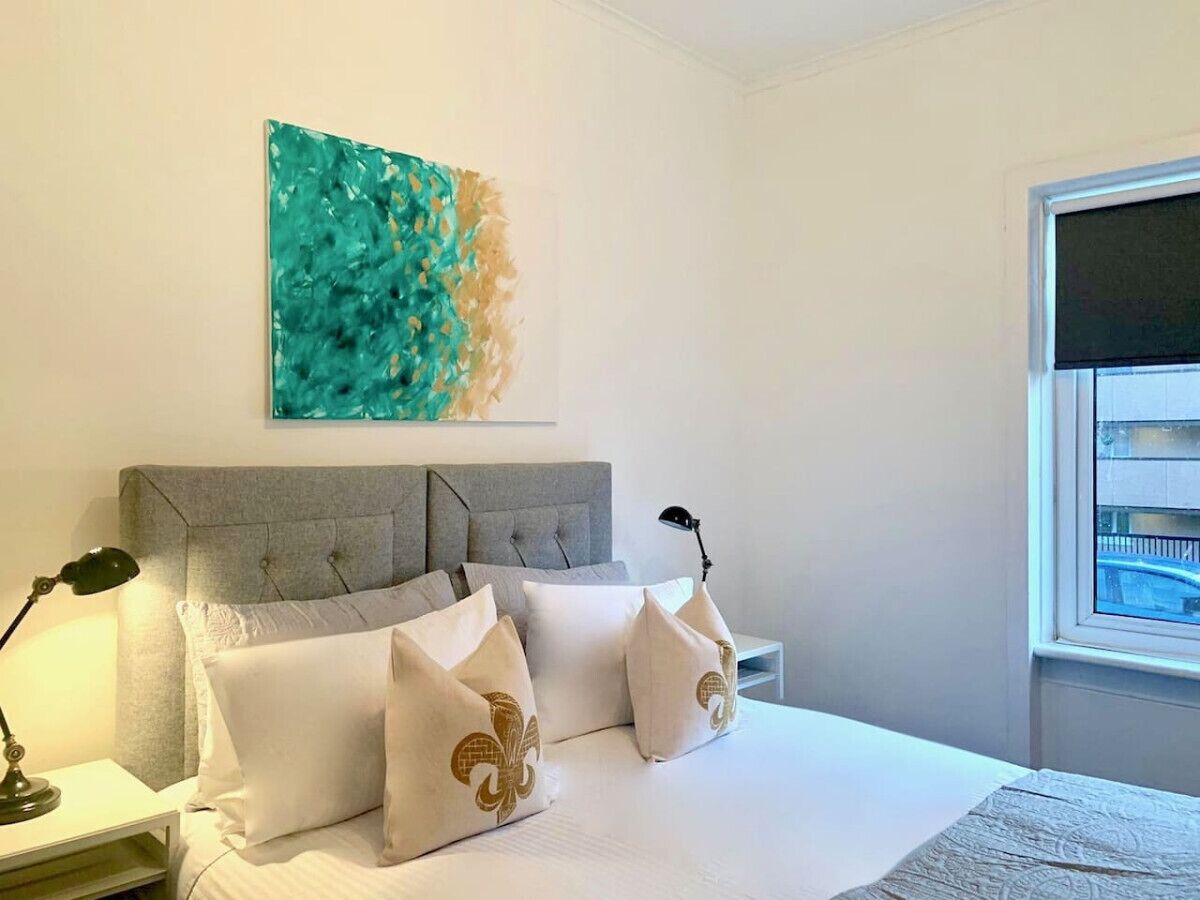 A bedroom with a grey upholstered headboard, white bedding, and a decorative wall piece above the bed.