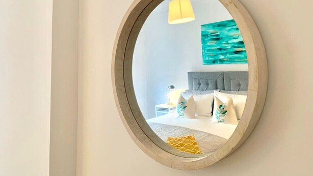 A bedroom with a round mirror, a bed with a grey headboard, and a painting of the sea on the wall. - Hillington Central - stylish 3 bedroom apartment (Glasgow)