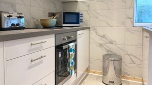 A modern kitchen with a microwave, toaster, oven, and a trash bin. - Hillington Central - stylish 3 bedroom apartment (Glasgow)