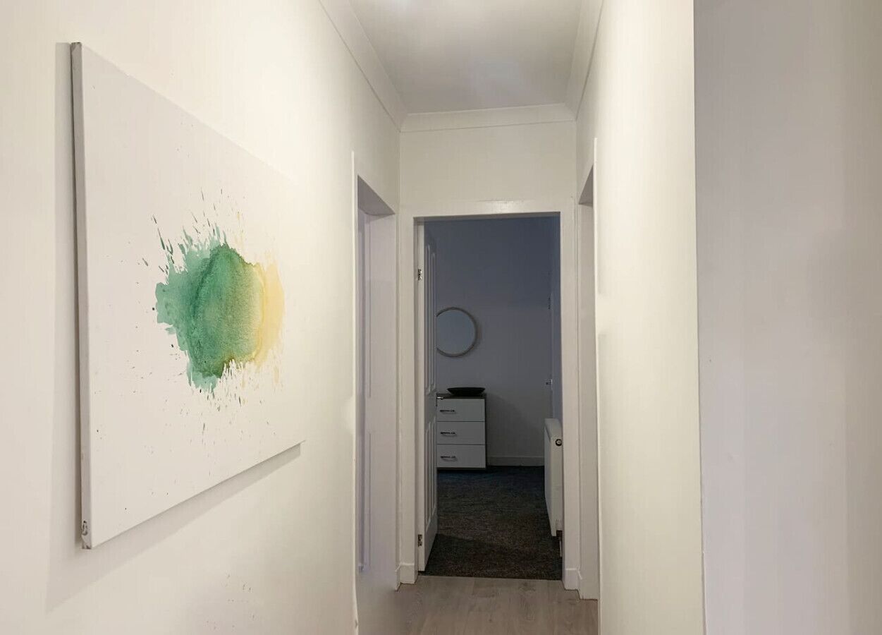 A hallway with a white wall and a door leading to a room with a round mirror and a small table.