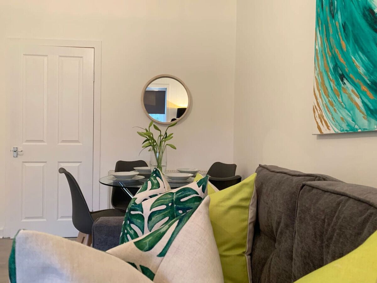 Ein Wohnzimmer mit grauem Sofa, einem runden Spiegel und einem Tisch mit Stühlen.