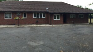 A single-story brick building with a flat roof, multiple windows, and a paved parking area.