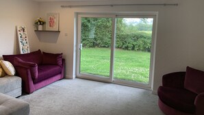 A room with a large sliding glass door leading to a grassy outdoor area. There is a purple sofa and a white sofa in the room.