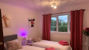 A hotel room with two beds, a window with red curtains, a radiator, and wall art including a giraffe and a cow.