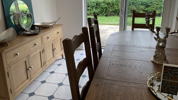 A dining area with a wooden table, chairs, a cabinet with decorative items, and a view of greenery through a glass door.