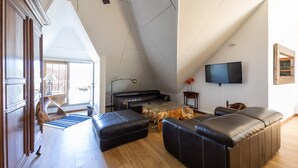 Un soggiorno moderno con soffitto alto, un divano in pelle nera, un tavolino in vetro e un televisore a schermo piatto montato a parete.