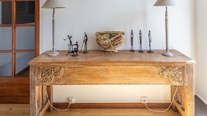 Un tavolo di legno con un cesto intrecciato e delle figurine, una lampada e un oggetto circolare fissato al muro in una stanza con pavimento in legno e soffitto spiovente.