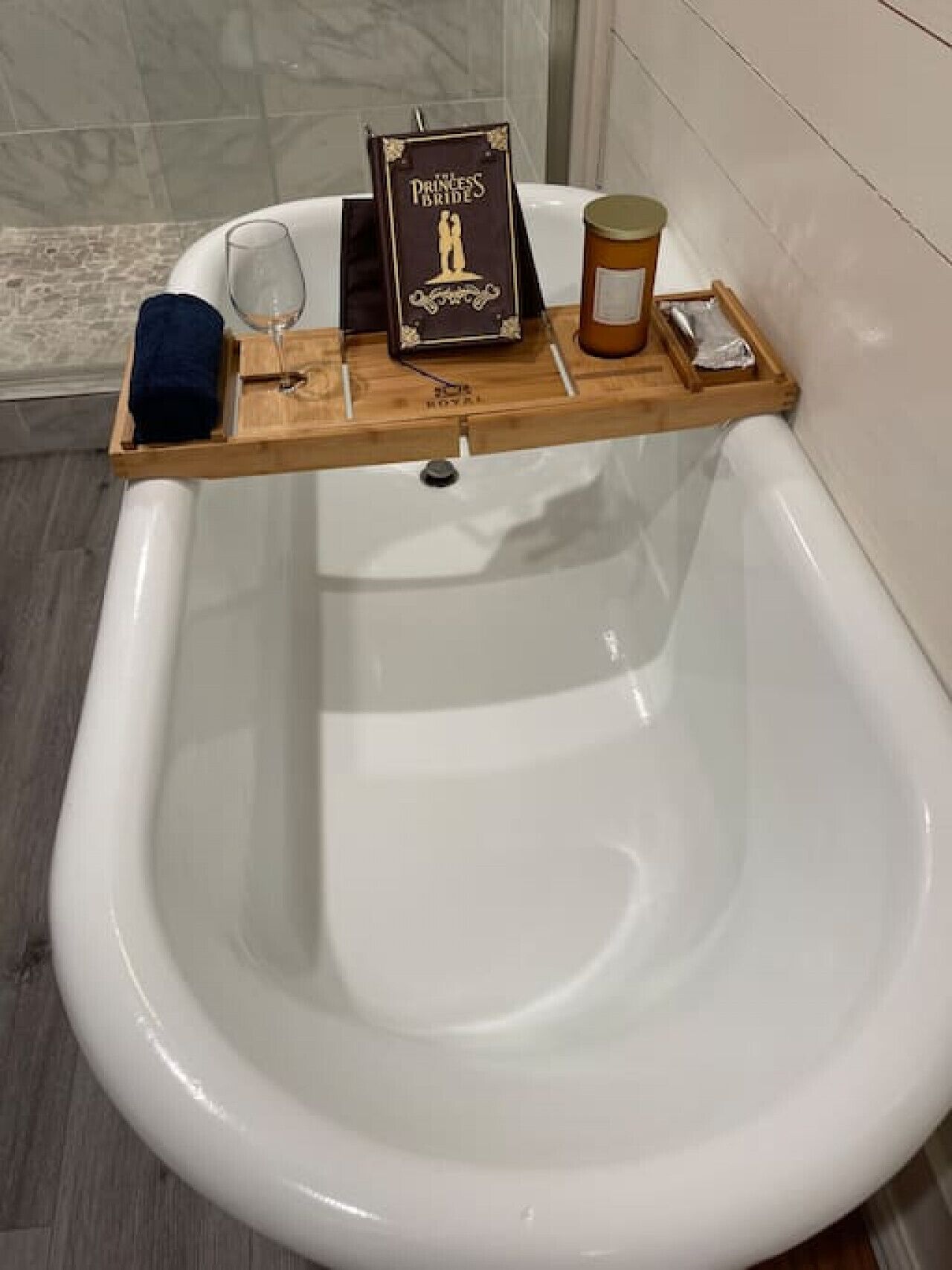 A bathtub with a wooden tray holding a candle, a glass, and a book titled "The Princess Bride".