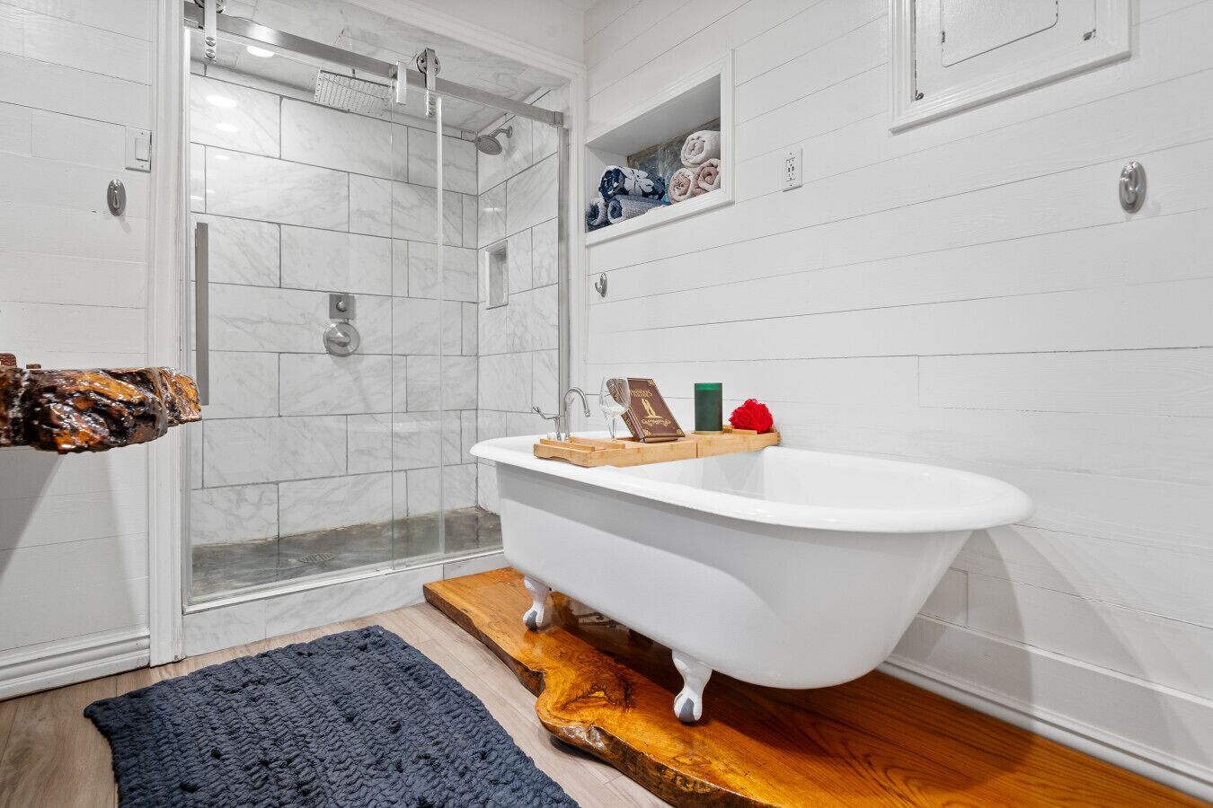 Ein Badezimmer mit einer freistehenden Badewanne, einer Duschkabine aus Glas und einer Holzbadematte.